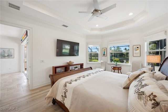 bedroom with ornamental molding, light hardwood / wood-style floors, ceiling fan, and a tray ceiling