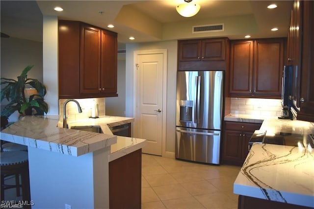 kitchen with tasteful backsplash, a raised ceiling, kitchen peninsula, stainless steel fridge, and a breakfast bar