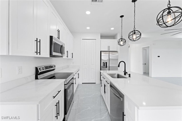 kitchen with a center island with sink, sink, hanging light fixtures, appliances with stainless steel finishes, and white cabinetry