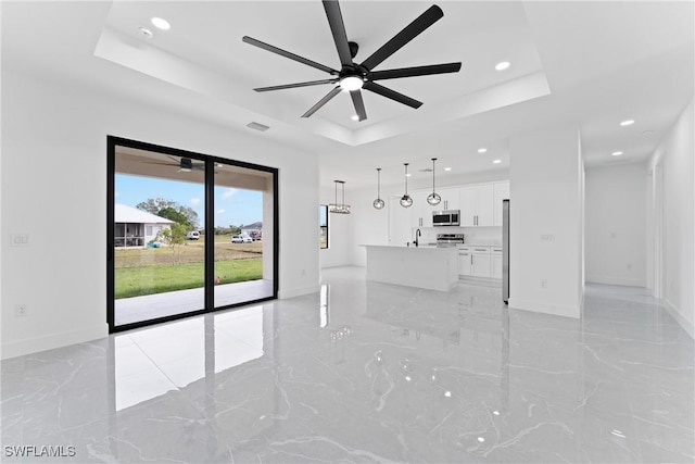 unfurnished living room featuring a tray ceiling, ceiling fan, and sink