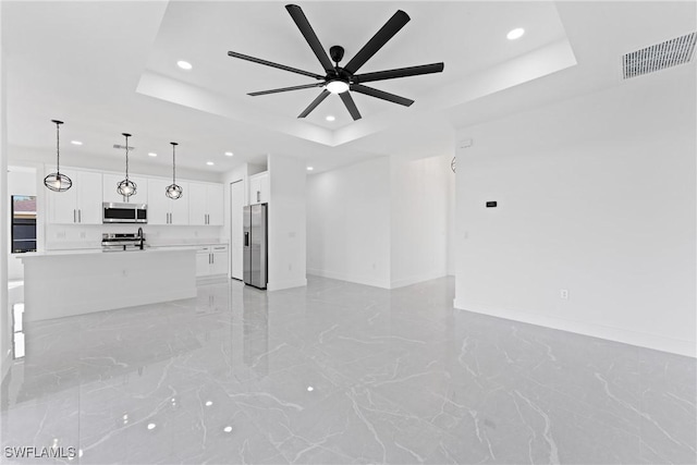 unfurnished living room featuring ceiling fan, sink, and a tray ceiling