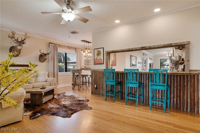 bar featuring ornamental molding, ceiling fan with notable chandelier, a textured ceiling, pendant lighting, and hardwood / wood-style flooring