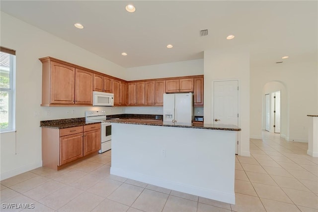 kitchen featuring light tile patterned floors, white appliances, an island with sink, and dark stone counters