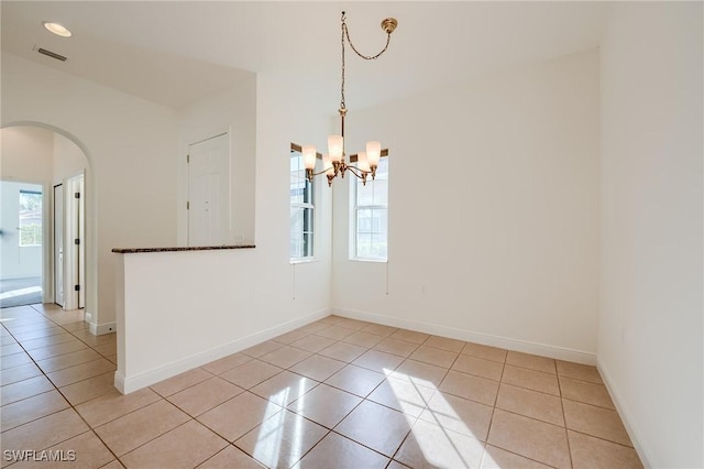 tiled spare room featuring a chandelier