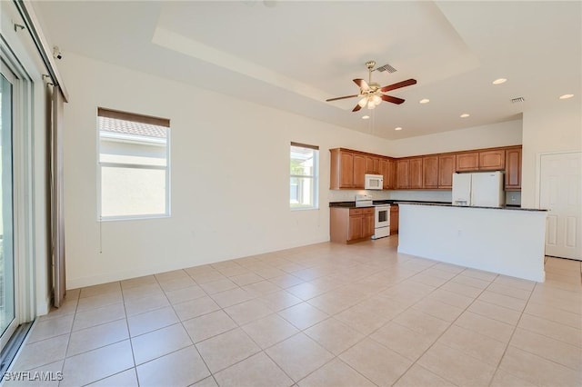 kitchen with a center island, white appliances, light tile patterned floors, and a tray ceiling