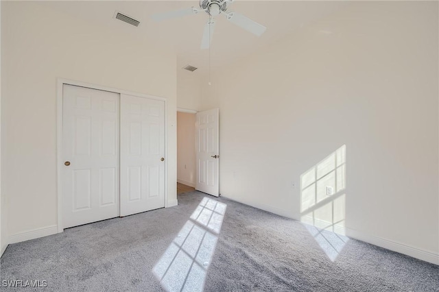 unfurnished bedroom featuring ceiling fan, light colored carpet, a towering ceiling, and a closet