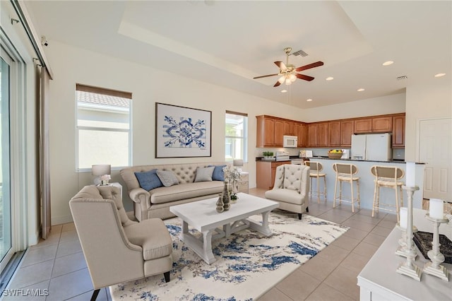 living room with light tile patterned floors, a raised ceiling, and ceiling fan