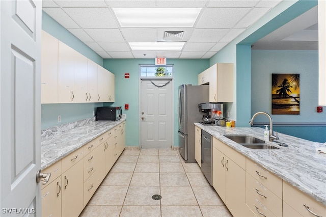 kitchen with sink, light stone counters, a paneled ceiling, light tile patterned floors, and appliances with stainless steel finishes