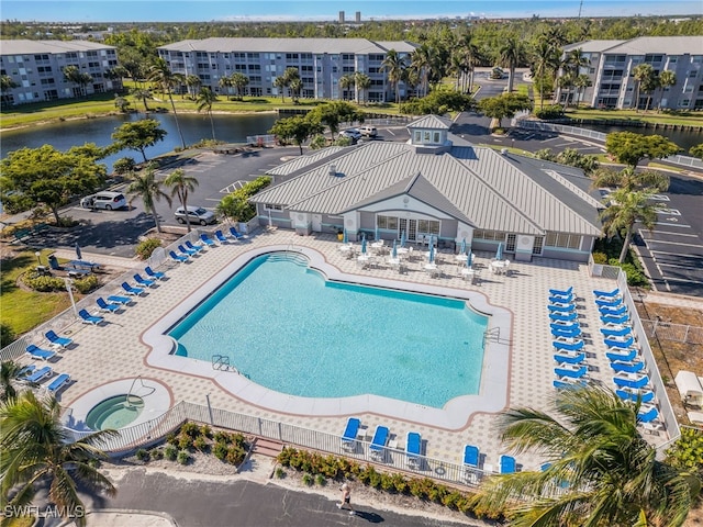 community pool featuring a water view, fence, a patio, and a hot tub