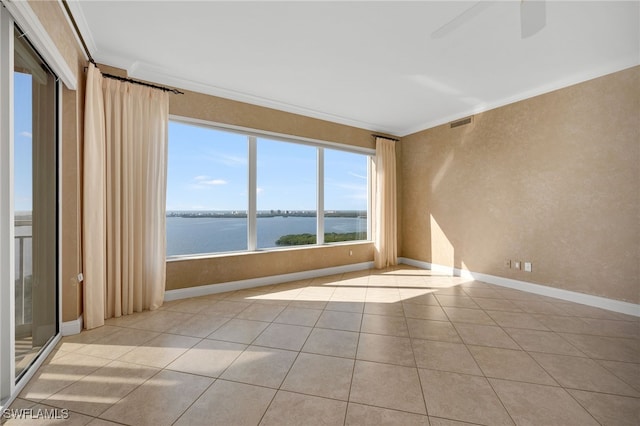 empty room with tile patterned floors, visible vents, a water view, ornamental molding, and baseboards