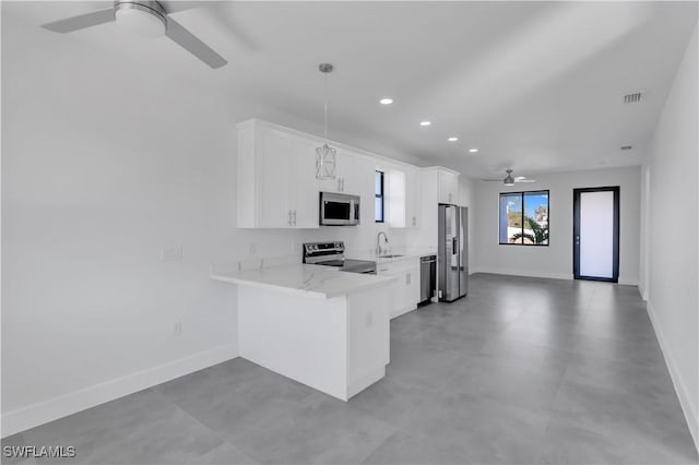 kitchen featuring decorative light fixtures, kitchen peninsula, white cabinetry, appliances with stainless steel finishes, and light stone counters