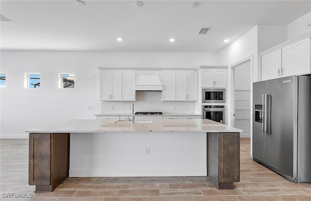 kitchen featuring tasteful backsplash, white cabinetry, an island with sink, and appliances with stainless steel finishes