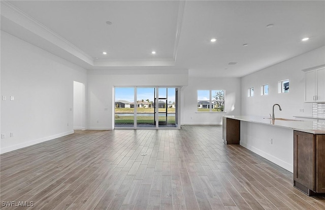 unfurnished living room featuring a tray ceiling, crown molding, sink, and hardwood / wood-style floors