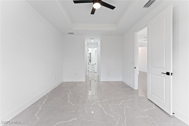 empty room with ceiling fan and a tray ceiling