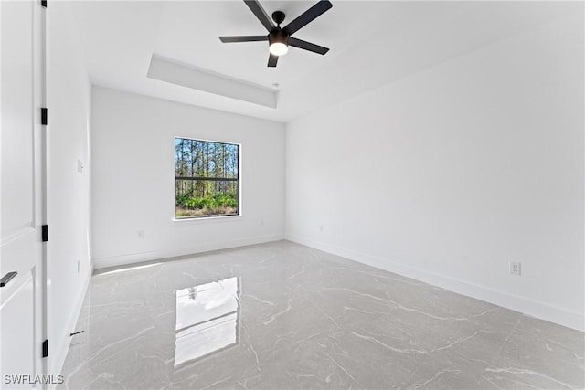 empty room with ceiling fan and a raised ceiling