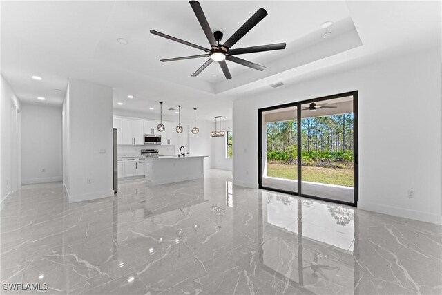 unfurnished living room featuring a tray ceiling, ceiling fan, and sink