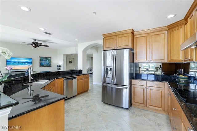 kitchen with kitchen peninsula, appliances with stainless steel finishes, dark stone counters, ceiling fan with notable chandelier, and sink