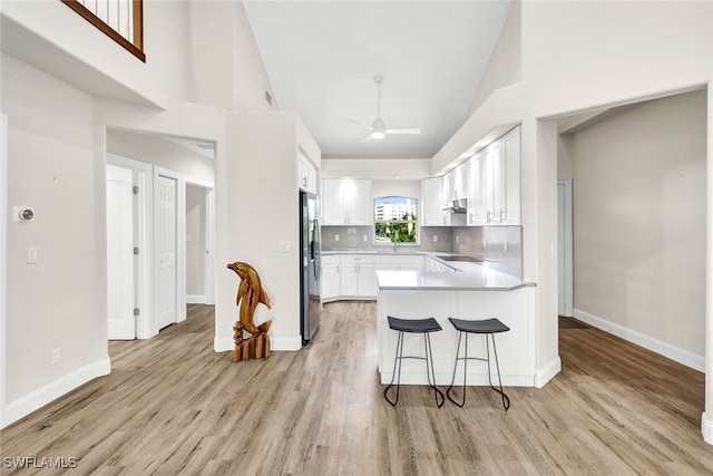 kitchen with tasteful backsplash, ceiling fan, stainless steel refrigerator, white cabinetry, and light hardwood / wood-style flooring