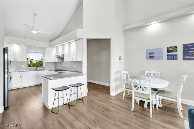 kitchen with kitchen peninsula, decorative backsplash, stainless steel refrigerator, white cabinetry, and high vaulted ceiling