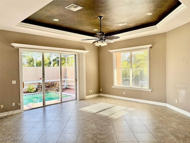 tiled empty room featuring a textured ceiling, a tray ceiling, ceiling fan, and ornamental molding