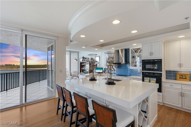 kitchen featuring backsplash, wall chimney exhaust hood, light countertops, and light wood finished floors