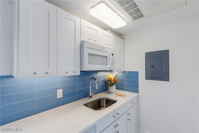 kitchen featuring white microwave, light countertops, electric panel, white cabinets, and a sink