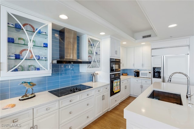 kitchen with visible vents, a sink, black appliances, light wood-style floors, and wall chimney exhaust hood