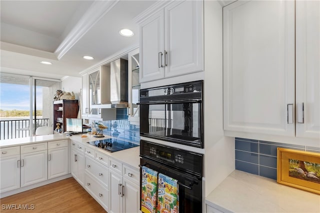 kitchen with black appliances, wall chimney range hood, tasteful backsplash, and white cabinets