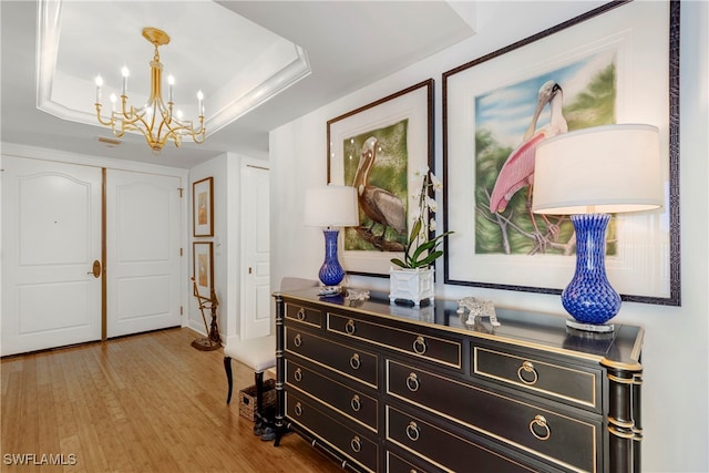 interior space with a closet, a raised ceiling, an inviting chandelier, and light wood finished floors