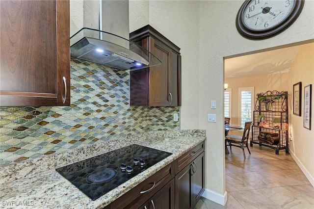 kitchen featuring light stone countertops, black electric stovetop, tasteful backsplash, wall chimney exhaust hood, and dark brown cabinetry