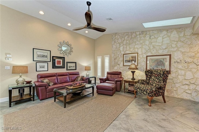 living room featuring a skylight, ceiling fan, high vaulted ceiling, and a textured ceiling