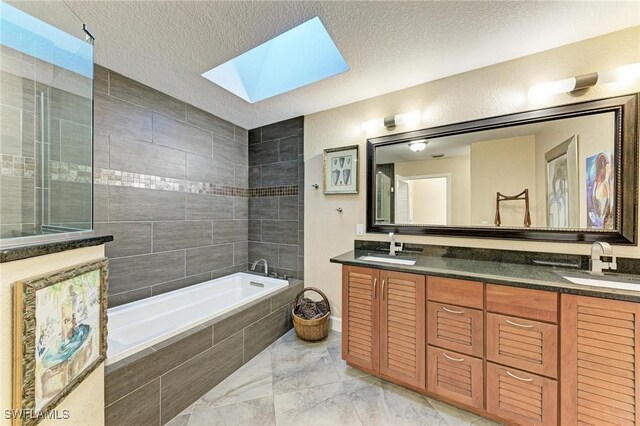 bathroom with a textured ceiling, vanity, a skylight, and tiled tub