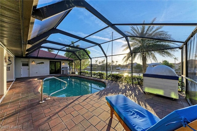 pool at dusk featuring glass enclosure, area for grilling, and a patio area