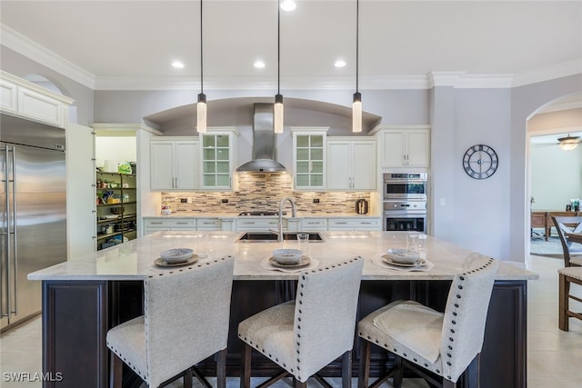 kitchen featuring pendant lighting, wall chimney exhaust hood, an island with sink, and appliances with stainless steel finishes