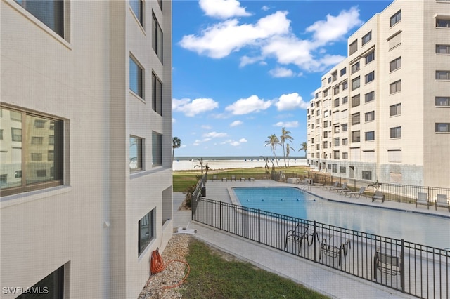 community pool with a patio area, a water view, and fence