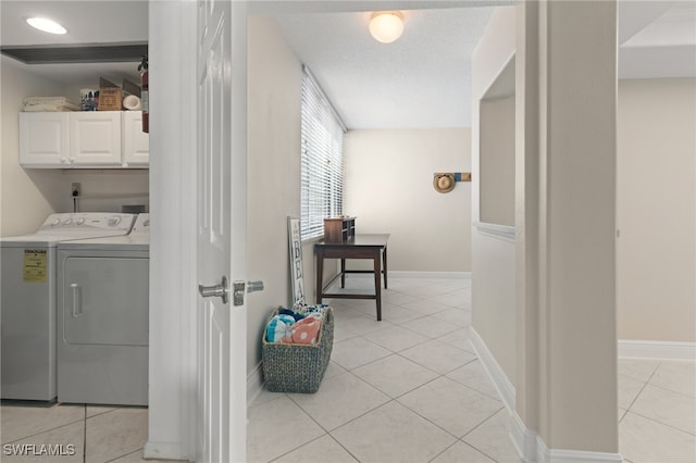 clothes washing area featuring cabinets, light tile patterned flooring, and washing machine and clothes dryer