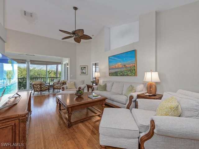 living room with ceiling fan, a towering ceiling, and light hardwood / wood-style flooring