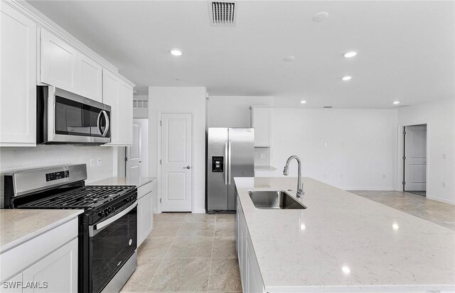 kitchen with stainless steel appliances, a sink, white cabinetry, decorative backsplash, and a center island with sink