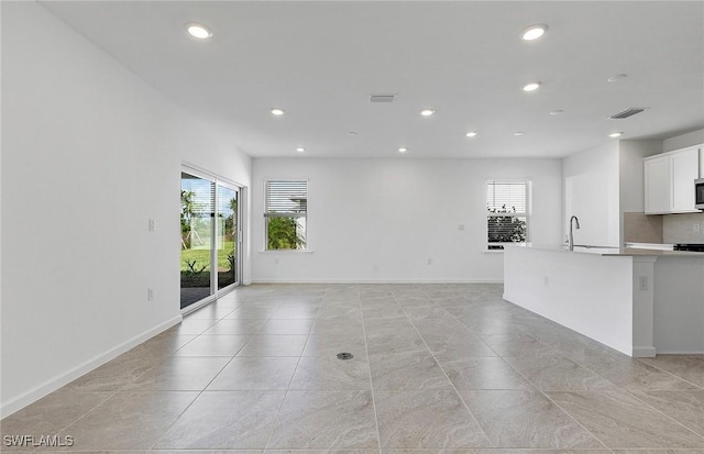 unfurnished living room with baseboards, a sink, visible vents, and recessed lighting