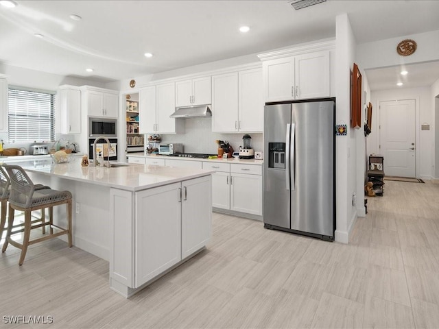 kitchen featuring appliances with stainless steel finishes, backsplash, a kitchen island with sink, sink, and white cabinetry