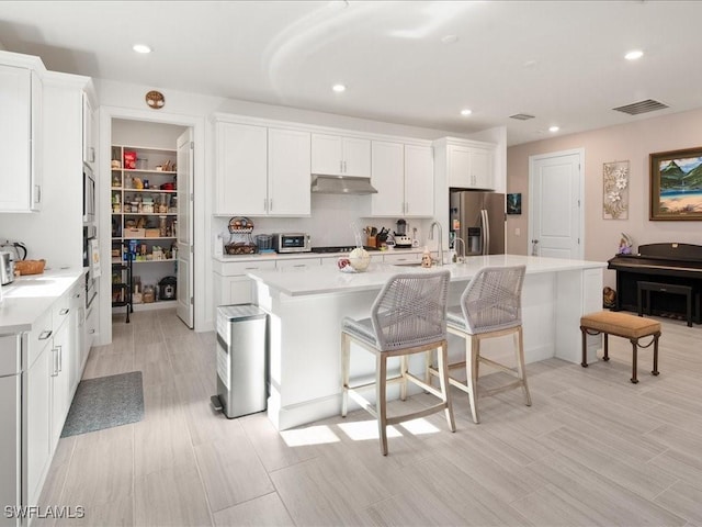 kitchen with stainless steel refrigerator with ice dispenser, white cabinetry, and an island with sink