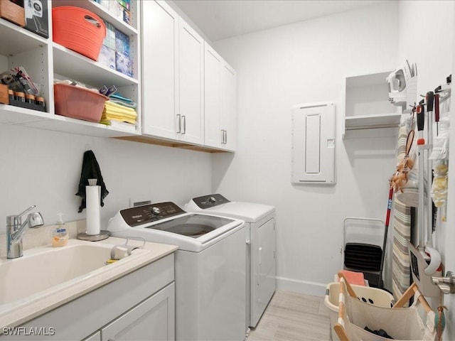 clothes washing area featuring washer and dryer, electric panel, cabinets, and sink