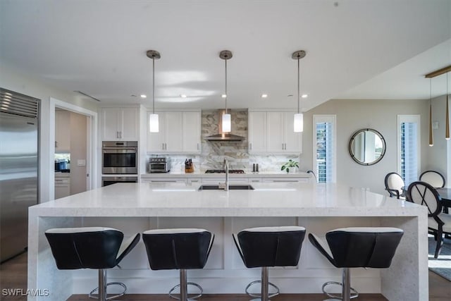 kitchen with wall chimney range hood, decorative light fixtures, appliances with stainless steel finishes, a large island, and white cabinetry