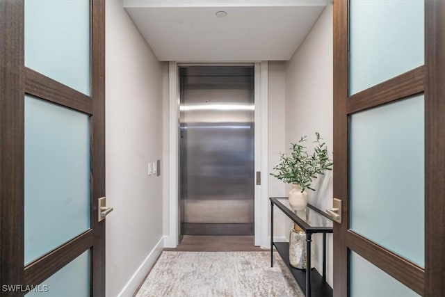 corridor featuring elevator and light hardwood / wood-style flooring