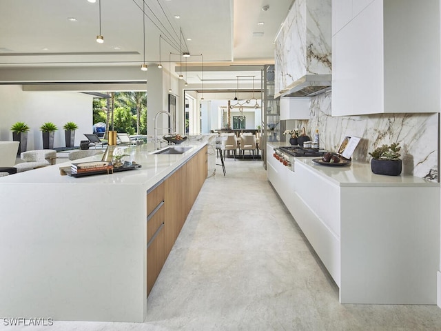 kitchen with sink, tasteful backsplash, hanging light fixtures, a large island with sink, and white cabinets