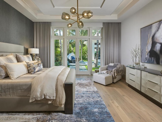 bedroom with access to exterior, a raised ceiling, light hardwood / wood-style floors, and a notable chandelier