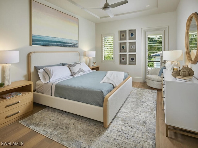 bedroom with a raised ceiling, ceiling fan, radiator heating unit, and light wood-type flooring