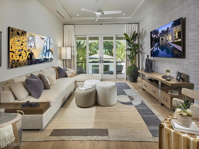 living room featuring light hardwood / wood-style flooring, a raised ceiling, ceiling fan, and french doors