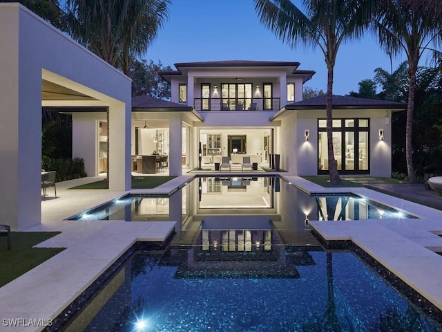 back house at dusk featuring a pool with hot tub, pool water feature, a patio, and a balcony