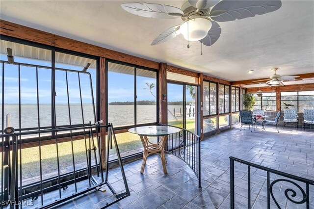 unfurnished sunroom featuring ceiling fan and a water view